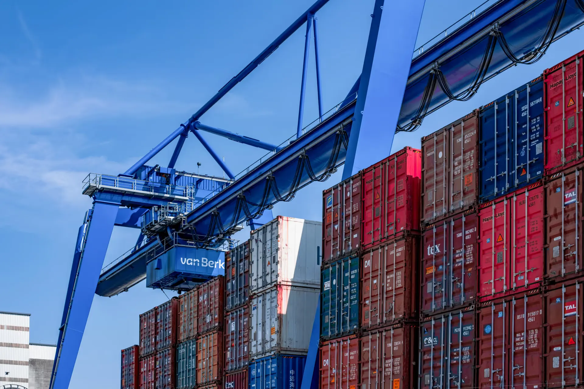 Blue cargo cranes above stacked shipping containers at a port terminal